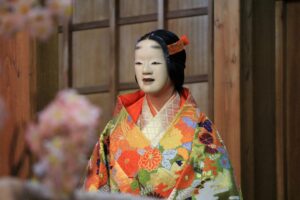 A Noh actress wearing a vibrant karaori robe and a traditional female mask, embodying the elegance and spiritual depth of classical Japanese theater.