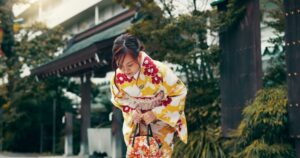 Gracefully bowing before a Shinto shrine, a young woman dressed in a traditional Japanese kimono