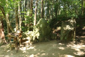 The entrance to Yomotsuhirasaka (the slope to the underworld) in Iya, Higashiizumo, Matsue City, Shimane Prefecture, featuring sacred rocks and a small wooden shrine surrounded by forest.