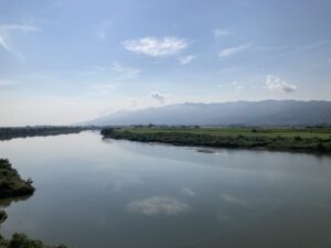 A calm view of the Chikugo River in Kyushu, Japan, with wide waters reflecting the sky and green fields stretching to the mountains—symbol of the historic irrigation project built through cooperation.