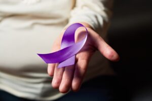 A hand holding a purple awareness ribbon, symbol of World Leprosy Day, representing compassion, dignity, and hope.
