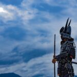 A solitary samurai in traditional armor stands quietly under a vast, cloud-filled sky, holding a spear and sword, symbolizing discipline, responsibility, and ethical resolve rather than aggression.